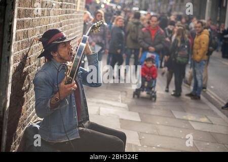 Un impersonator Jimi Hendrix jouant de la guitare avec ses dents avec une foule regardant, Brick Lane, Londres Banque D'Images