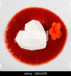 Dessert mousse blanc en forme de coeur avec sauce aux fruits rouges dans une assiette. Banque D'Images