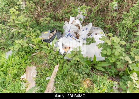 Sacs à bout de vol de déchets de construction sur le côté d'une route de campagne, Royaume-Uni. Métaphore pollution environnementale, déchets plastiques, déchets ruraux, pourboire des mouches. Banque D'Images