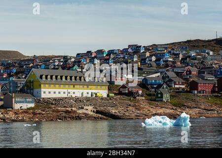 Maisons traditionnelles dans la baie d'Upernavik avec un grand bâtiment public jaune, avec iceberg en première ligne Banque D'Images