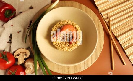 Soupe épicée de nouilles instantanées aux crevettes et légumes. Soupe de crevettes, cuisine, nourriture. Vermicelles séchées en forme de cercle dans une assiette. Pâtes, pour le prepar Banque D'Images