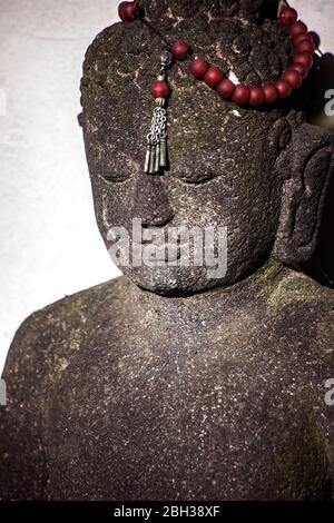 statue de bouddha en pierre avec perles de prière rouges Banque D'Images
