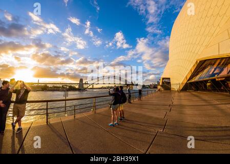 Sydney, Australie. Les touristes et les habitants de la région apprécient le coucher du soleil lors d'une chaude soirée d'été près de l'Opéra. Dans le contexte le pont du port. Banque D'Images