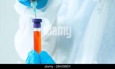 Vue rapprochée du médecin dans un costume de bioprotection et des gants bleus prenant un échantillon sanguin dans un tube à essai avec une seringue sur fond blanc Banque D'Images