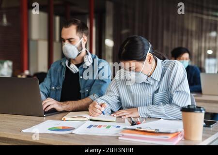 Photo d'étudiants multinationaux focalisés dans des masques médicaux étudiant avec ordinateur portable en classe Banque D'Images