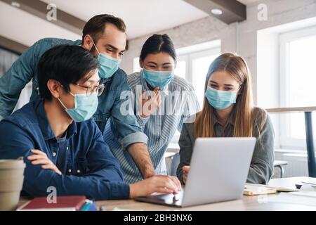 Photo de multinationales a accueilli des étudiants en masques médicaux étudiant avec un ordinateur portable en classe Banque D'Images