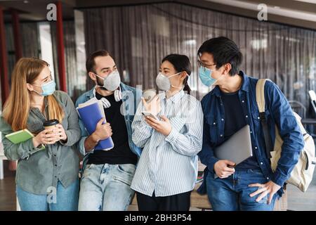 Photo d'étudiants multinationaux joyeux dans des masques médicaux parlant en classe Banque D'Images