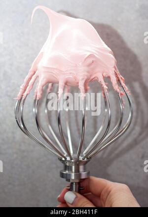 Crème meringue suisse fouettée rose sur le dessus du grand batteur en métal. Fond gris clair. Banque D'Images