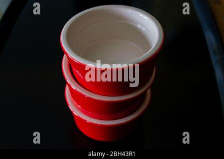 Trois ramequins rouges avec un intérieur blanc empilés l'un sur l'autre et placés sur un plateau noir Banque D'Images