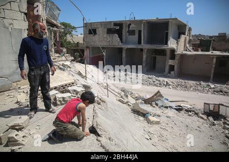 Idlib, Smali, Syrie. 23 avril 2020. Un père et son jeune fils dans leur maison endommagée, après un calme dans les combats dans le nord de la Syrie. Les gens sont revenus vivre en ruines par crainte de la propagation du coronavirus dans les camps de déplacement.vie quotidienne à la lumière de la prévalence du coronavirus dans les zones du conflit syrien. Après neuf ans de guerre, la Syrie est divisée en trois parties rivales incapables de travailler ensemble et mal préparées à faire face au coronavirus Covid19. Crédit: Mouneb AIM/ZUMA Wire/Alay Live News Banque D'Images