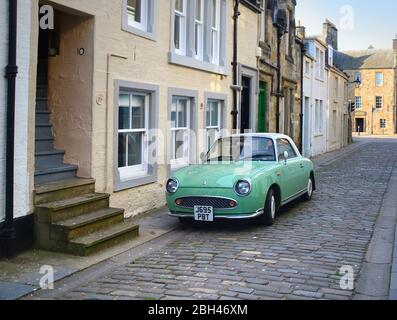 La voiture rétro des années 1960, la Nissan Figaro stationné dans une rue pavée de la vieille ville de St andrews, cinquife, en Écosse Banque D'Images