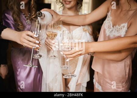 Les mains féminines tiennent des verres de champagne à la fête des poules. Mariée et bridesmaids toaster avec champagne et s'amuser le matin du mariage. Gros plan Banque D'Images