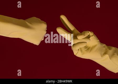 Mains avec gants jaunes jouant du papier de roche ou des ciseaux en temps de coronavirus. Photo avec espace de copie. Banque D'Images