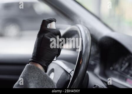 Mains féminines dans des gants de protection en caoutchouc désinfectant l'intérieur de la voiture pour la protection contre la contagion du virus. Nettoyage de la direction de voiture, pulvérisation de désinfectant liq Banque D'Images