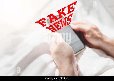 Fausses nouvelles infodemics pendant le concept de pandémie de Covid-19. Les mains de l'homme tenant le téléphone mobile lire les nouvelles mondiales ou le réseau social à la maison. Lire la dernière actualité Banque D'Images