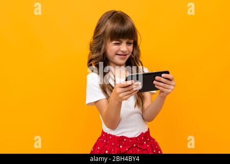 Portrait de charmante fille caucasienne avec de longs cheveux de châtaigniers et un joli visage en robe blanche et rouge montre un film ou des dessins animés avec son téléphone et son malle Banque D'Images