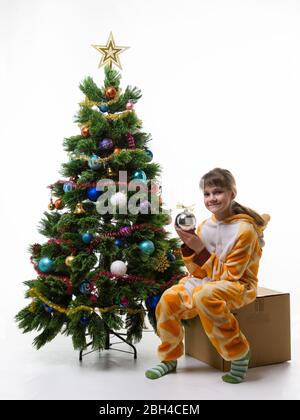 Une fille est assise sur une boîte pour stocker des décorations de Noël et tient une balle dans ses mains Banque D'Images