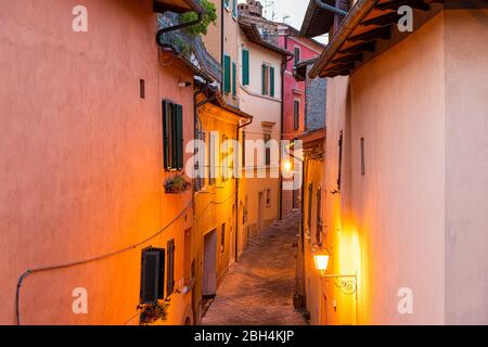 Chiusi, Italie rue vide ruelle étroite dans le petit village historique de Toscane pendant la nuit d'été avec personne, orange lampe jaune ilumina Banque D'Images