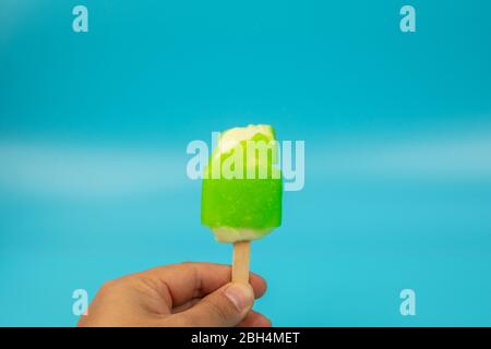 Main de l'homme tenant la crème glacée Popsicle citron goût sur fond bleu. Banque D'Images