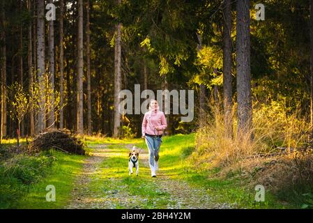 Jeune femme et chien courant ensemble dans le pays en forêt. Gai femme exerçant en plein air avec son animal de compagnie. Banque D'Images