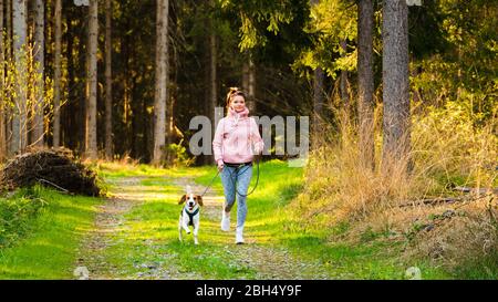 Jeune femme et chien courant ensemble dans le pays en forêt. Gai femme exerçant en plein air avec son animal de compagnie. Banque D'Images