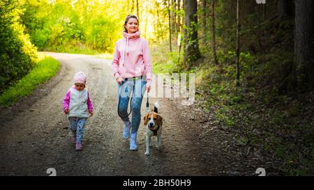 Jeune mère avec enfant et chien marchant ensemble sur le chemin du pays dans la forêt. Gai 2 ans en plein air. Banque D'Images