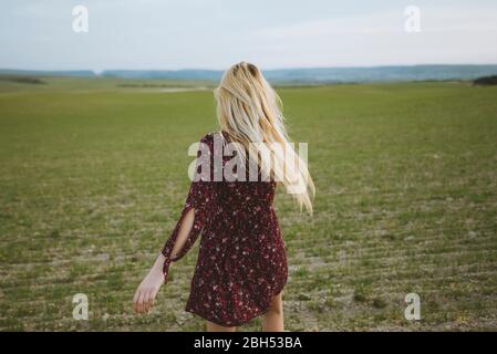 Jeune femme blonde caucasienne en robe courant au printemps au coucher du soleil Banque D'Images