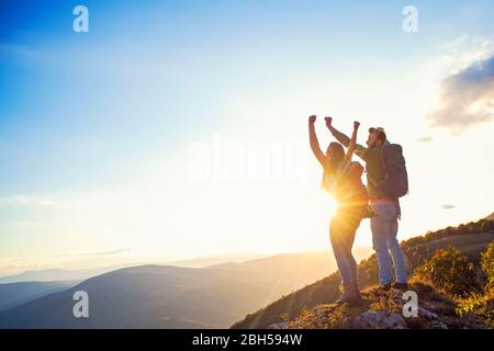 heureux couple homme et femme touriste au sommet de la montagne au coucher du soleil dehors pendant une randonnée en été Banque D'Images