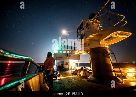 23 avril 2020, Schleswig-Holstein, Helgoland: Un scientifique se tient à la rampe du bateau de bouée pontant 'Lév Taifun' peu après le départ à Helgoland et regarde les étoiles. Le signal de départ pour un grand champ d'essais maritimes au large de Helgoland: Les scientifiques du Centre d'essais des technologies maritimes ont utilisé des barils pour marquer une superficie de trois millions de mètres carrés non loin de l'île de la mer du Nord. Il est destiné à fournir des installations d'essai pour la robotique maritime à l'avenir. Les fabricants et les scientifiques peuvent y tester différents scénarios. Par exemple, vehic autonome sous-marin Banque D'Images