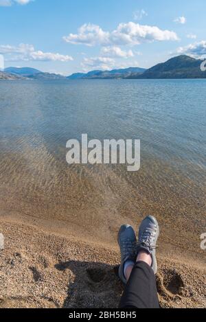 Pieds de femme en chaussures de randonnée en premier plan avec vue sur le lac et les montagnes dans la vallée de l'Okanagan Banque D'Images