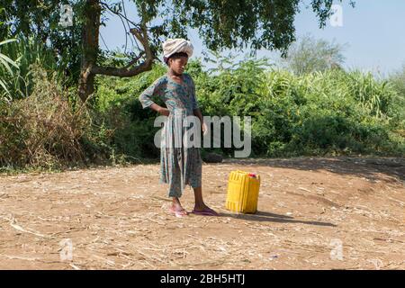 Une jeune femme s'arrête et repose sur un pot lourd, jaune, en plastique rempli d'eau. En Ethiopie, Afrique. Banque D'Images