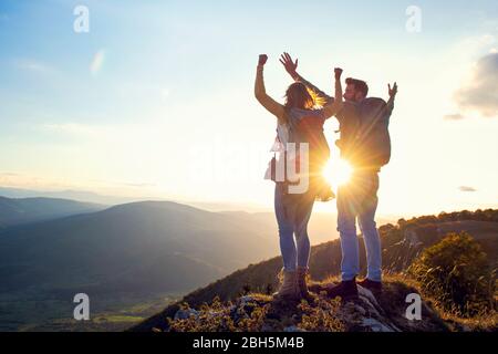 heureux couple homme et femme touriste au sommet de la montagne au coucher du soleil dehors pendant une randonnée en été Banque D'Images