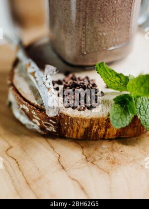 Secouez les protéines en bonne santé avec la banane, le beurre d'arachide, l'avoine et le sirop d'agave dans un verre élégant, décoré de protéines de chocolat, de flocons d'avoine et de menthe Banque D'Images