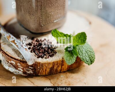 Secouez les protéines en bonne santé avec la banane, le beurre d'arachide, l'avoine et le sirop d'agave dans un verre élégant, décoré de protéines de chocolat, de flocons d'avoine et de menthe Banque D'Images