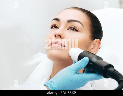 médecin faisant une thérapie par ondes acoustiques à une femme. Rajeunissement de la peau avec des ondes acoustiques, visage étroit Banque D'Images