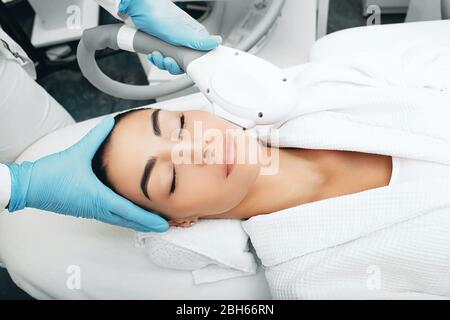 Femme brunette pendant élimine les taches brunes sur le visage, Beauticien utilisant la technologie de rajeunissement ELOS Banque D'Images