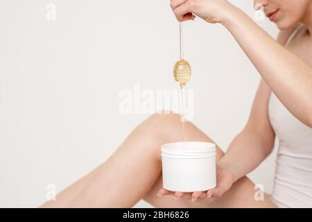 Femme tenant le bâton de miel qui coule vers le bas de cire liquide dans le récipient sur fond blanc. Banque D'Images