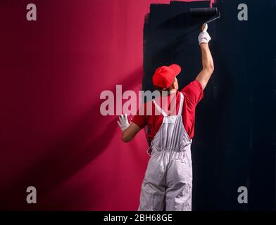 Homme peint un mur. Peintre en rouge mur de peinture en noir Banque D'Images