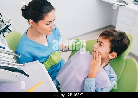 Tristesse petit garçon montrant la douleur dentaire à son dentiste. Il visite le dentiste pédiatre Banque D'Images