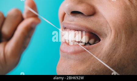 Bouche mâle rapprochée tout en flosant les dents avec fil dentaire sur fond bleu. Hygiène dentaire Banque D'Images