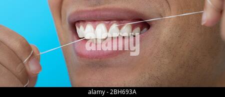 Bouche mâle rapprochée tout en flosant les dents avec fil dentaire sur fond bleu. Hygiène dentaire Banque D'Images