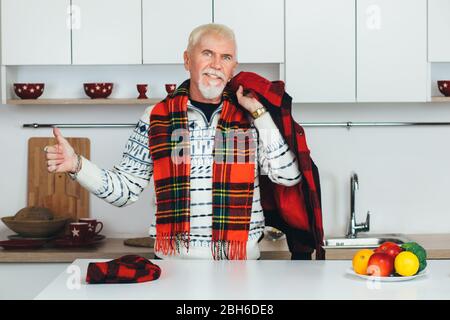 homme âgé montrant des pouces vers le haut, souriant regardant l'appareil photo et se tenant à la maison dans sa cuisine blanche. personnes âgées heureux à la maison Banque D'Images