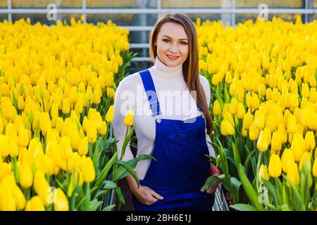 portrait de printemps d'une femme debout sur une plantation de fleurs avec tulipes souriant et regardant la caméra Banque D'Images