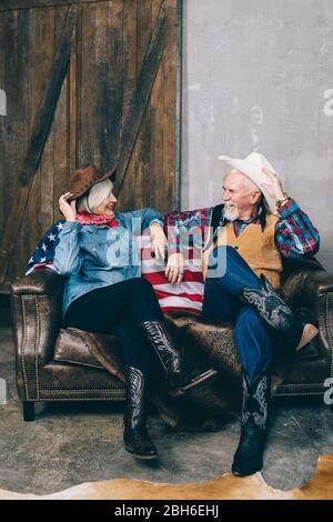 couple âgé vêtu de cowboy, assis sur le canapé, regardant l'un l'autre. Elégant aînés Banque D'Images