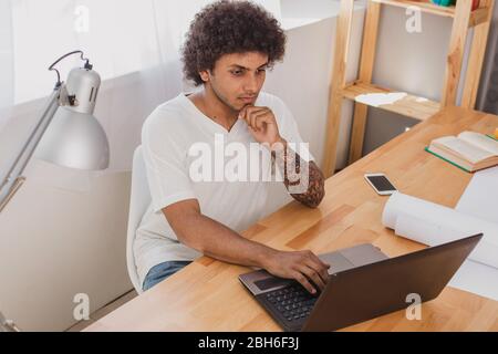 Travailler à domicile sur un ordinateur portable. L'homme séduisant de nationalité arabe a concentré ses efforts sur l'ordinateur portable et la pensée. Banque D'Images