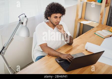 Étudier chez vous sur un ordinateur portable. Homme séduisant concentré regardant l'ordinateur portable et la pensée. Banque D'Images