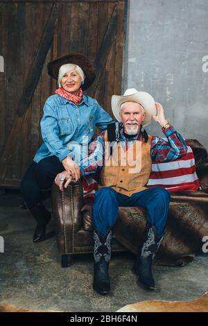 couple âgé vêtu de cowboy, assis sur le canapé, regardant l'un l'autre. Elégant aînés Banque D'Images