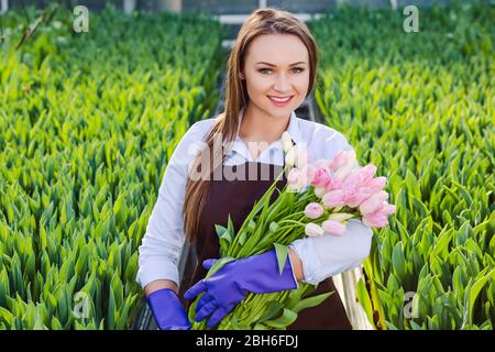 Fleuriste de jardinier de femme tenant un bouquet de fleurs, debout dans une serre, où les tulipes cultivent Banque D'Images