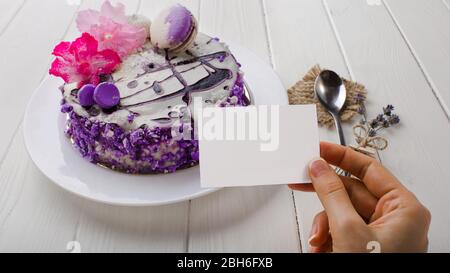 gros plan, main femelle tenant vide blanc sur fond de gâteau avec une fleur sur table en bois blanc . Vue de dessus Banque D'Images