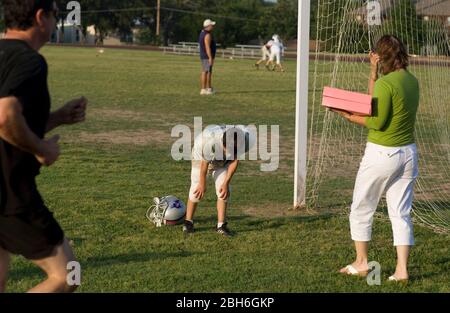 Austin, Texas États-Unis, 23 mai 2009: Un jeune joueur de football épuisé se déplace hors du terrain après la pratique alors que sa mère approche à un printemps après l'école pratique. ©Bob Daemmrich Banque D'Images